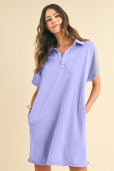 A woman wearing a blue purple mineral-washed Johnny collar short sleeve dress with a relaxed fit and pockets, styled for a casual and effortless look.  She has her hands in her pcoket.