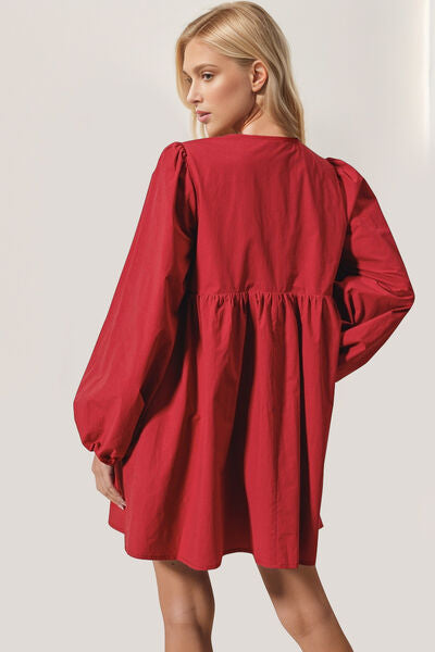 The back of a woman wearing a red tie-front mini dress with long puff sleeves, standing in natural light.