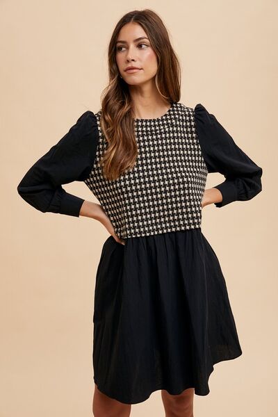 Front view of a tie-back plaid mini dress with long sleeves and a houndstooth bodice, styled with a relaxed fit and hands on hips for a confident pose.