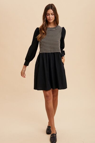 Full front view of a tie-back plaid mini dress featuring a houndstooth bodice, long sleeves, and a flowy skirt, styled with black loafers for a polished look.